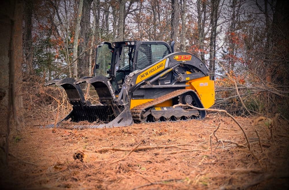 New Holland skid steer loader with grapple attachment in a wooded clearing.