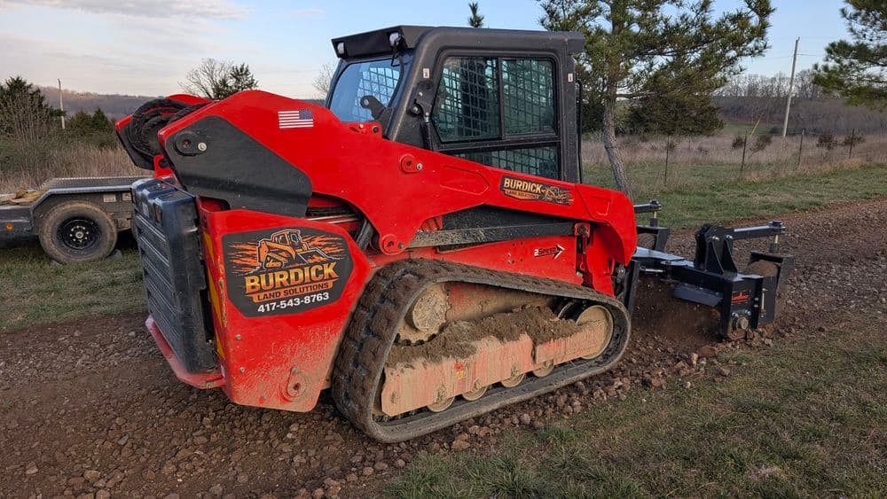 Burdick Land Solutions red skid steer loader on a dirt path, ready for landscaping tasks.