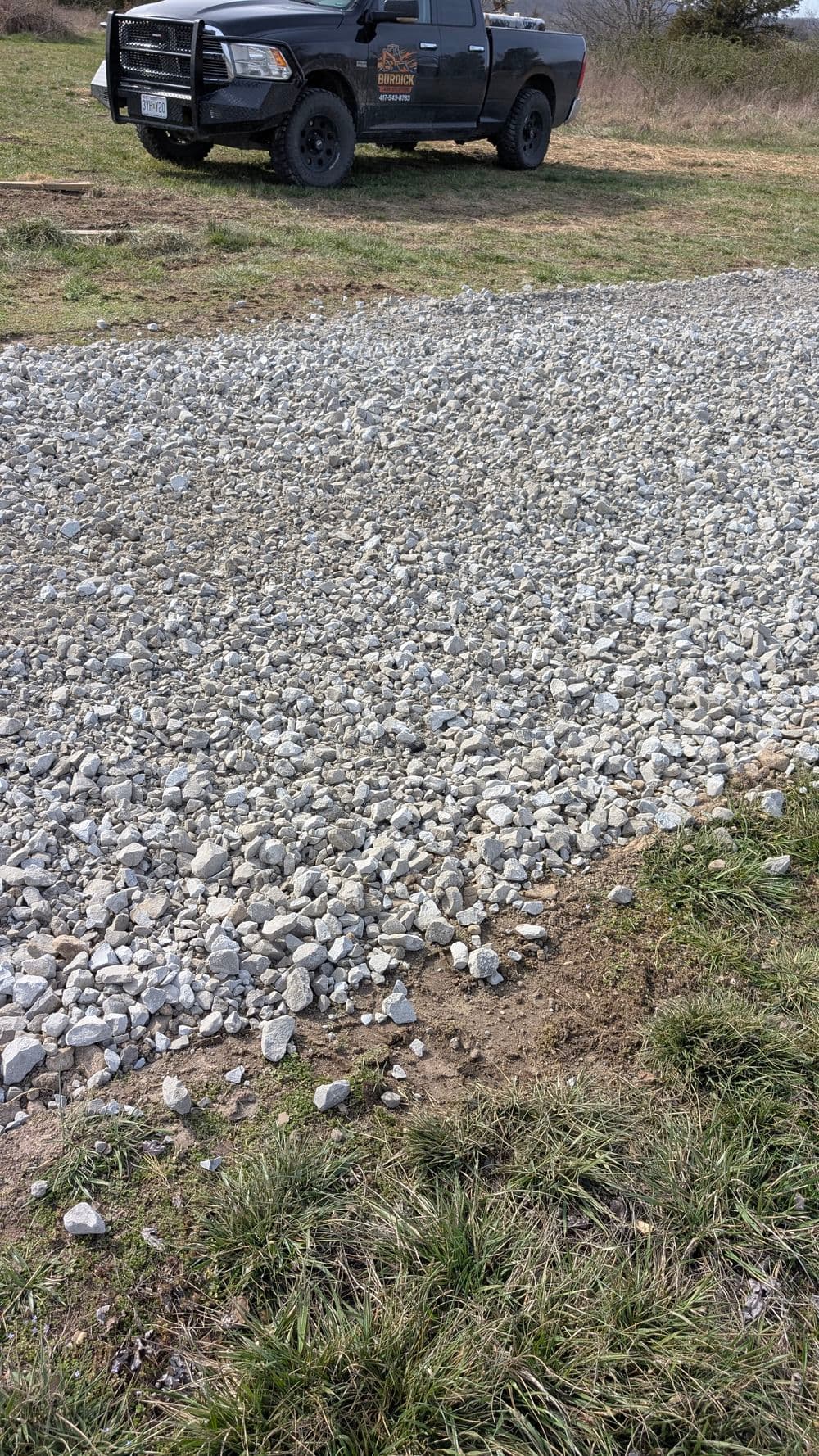 Gravel driveway with a parked black truck in the background on a rural property.