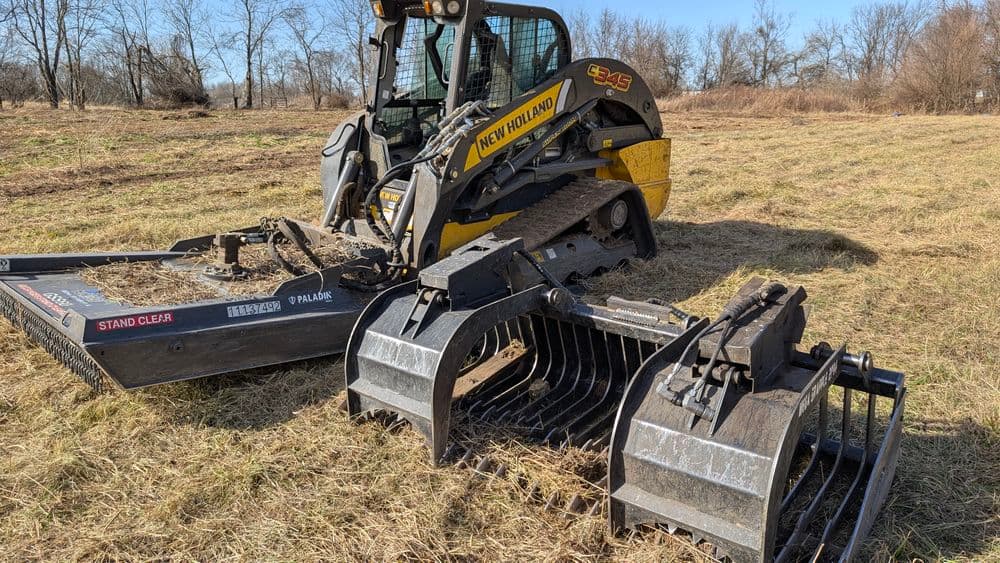 New Holland skid loader with grapple attachment working on a grassy field.