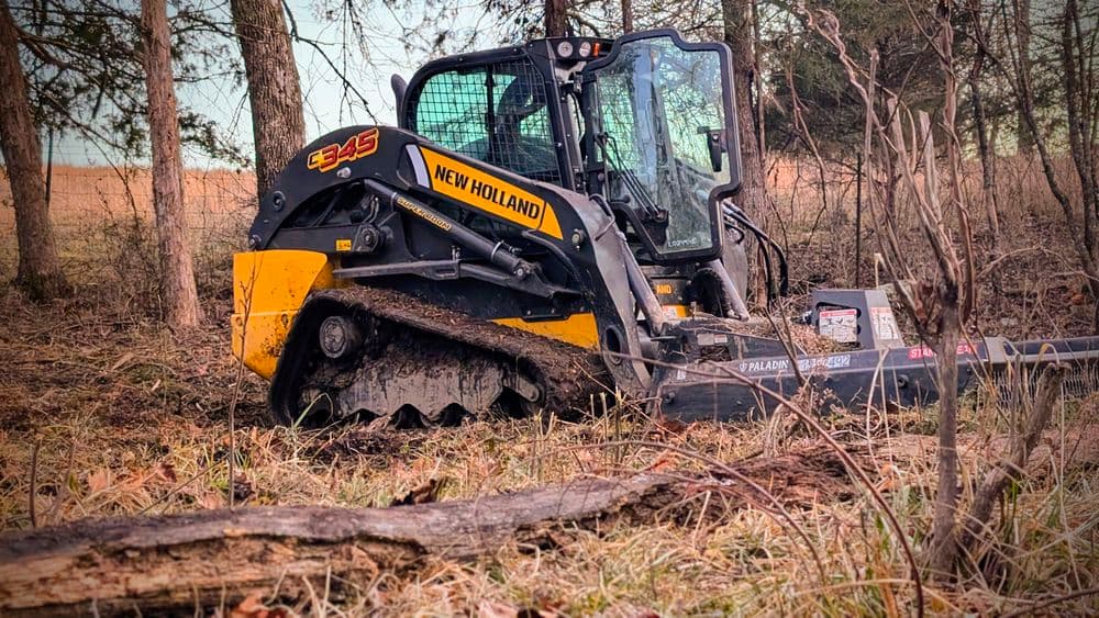 New Holland E345 compact track loader in a forested area, ideal for land clearing and construction.