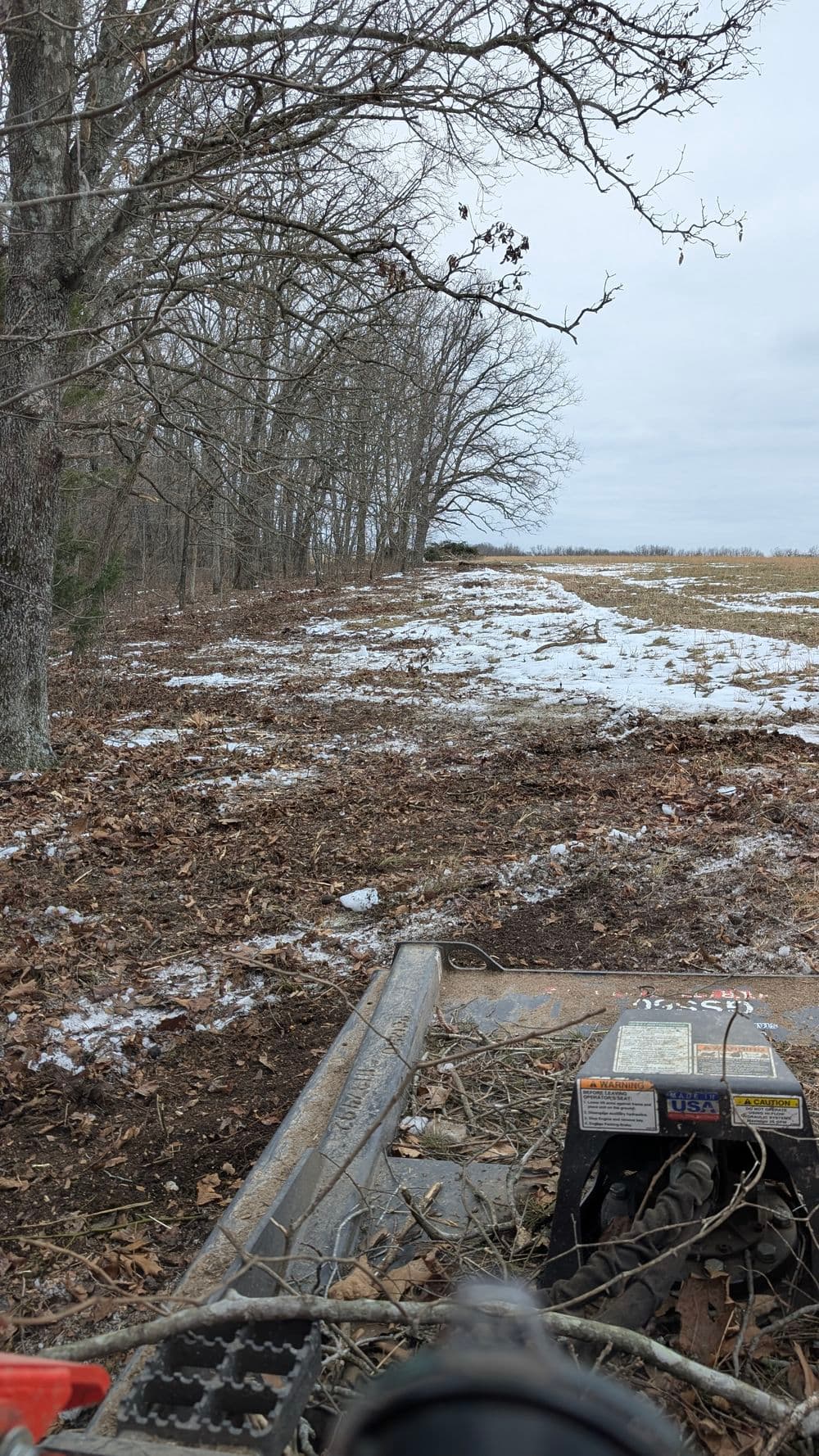 View from a mower on a snowy path lined with trees, showing cleared leaves and dirt.