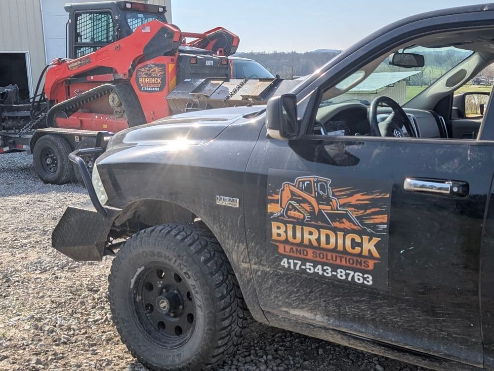 Burdick Land Solutions truck and skid steer at a construction site, showcasing landscaping equipment.
