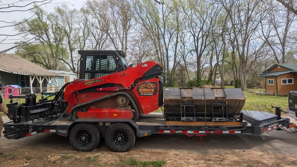 Bobcat skid steer loader on a trailer ready for construction work in wooded area.
